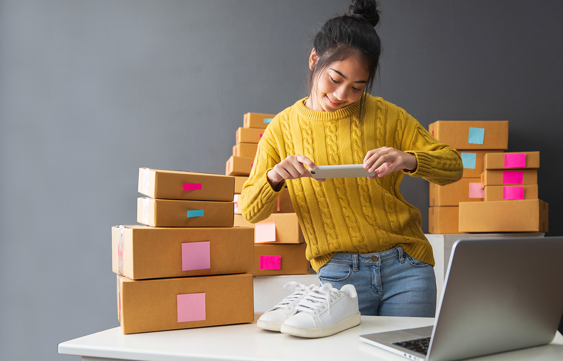 Femme prenant une photo de chaussures pour les vendre en ligne, avec des boîtes derrière elle