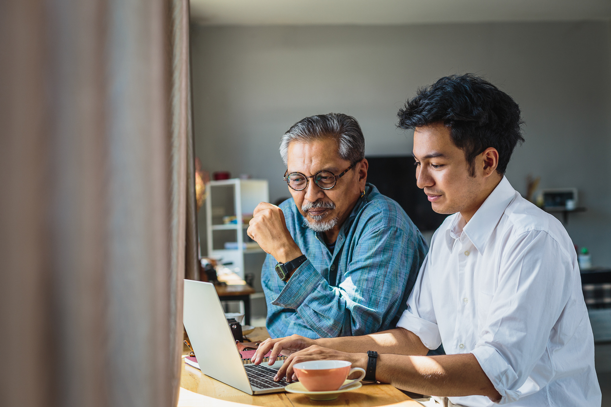 Older and younger man sitting at desk with laptop computer